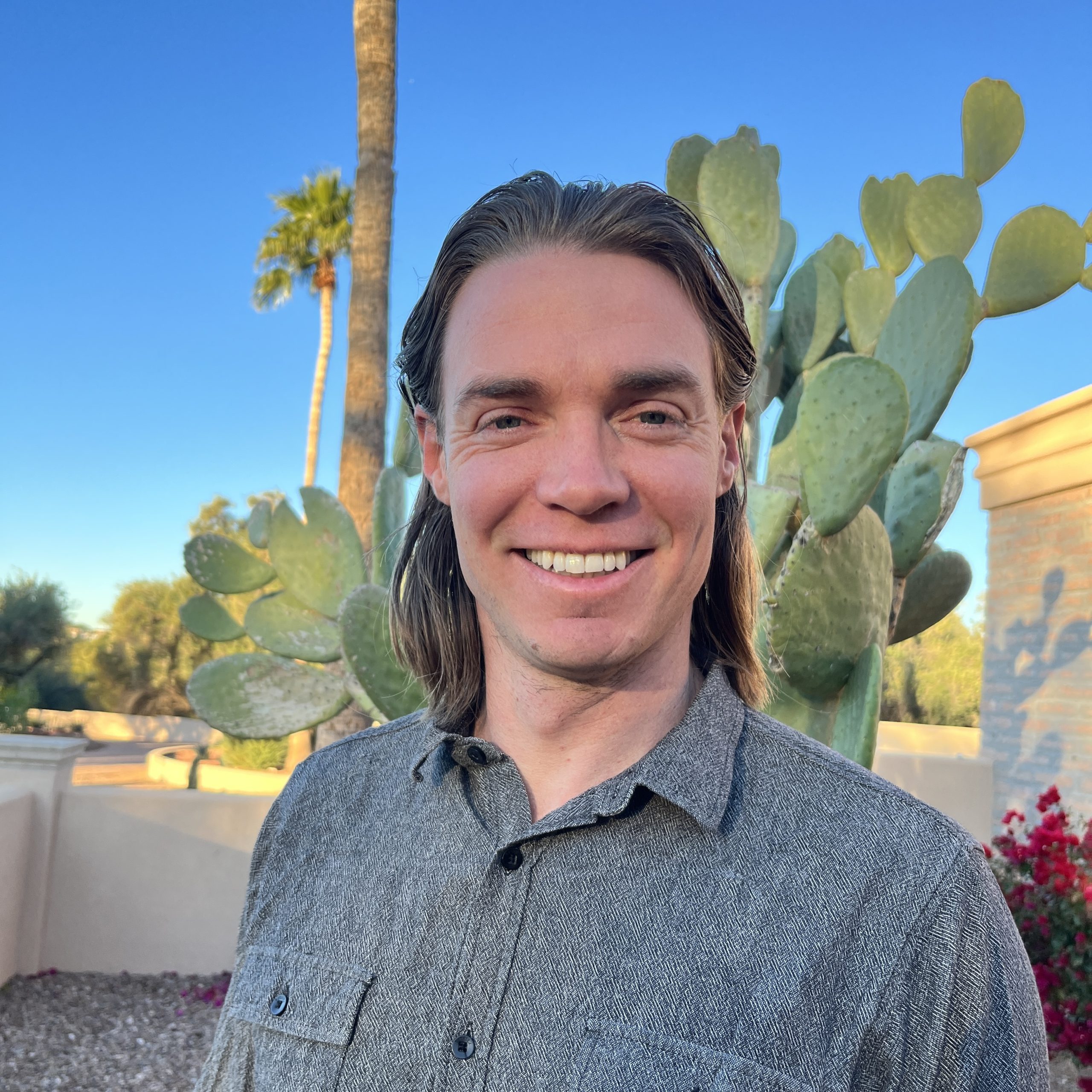 A man with long hair standing in front of a cactus.